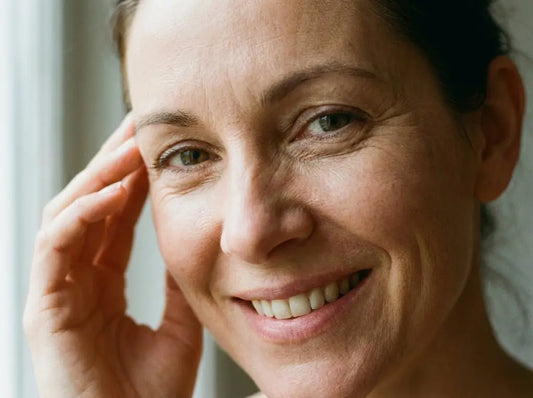A middle-aged woman with firm, healthy under-eye skin smiling naturally, representing the effects of peptide eye cream.